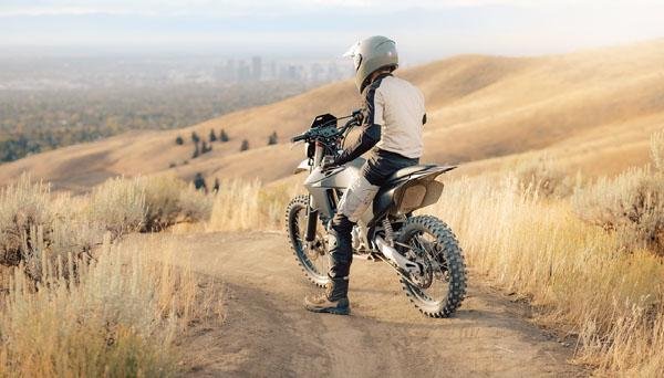 An electric off-road motorcycle rider stopped on a designated dirt trail overlooking Boise from the foothills.
