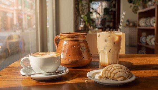 Mexican-inspired coffee drinks, a clay mug and pan dulce on a café table in a warm downtown coffee shop.